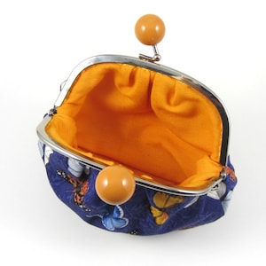 May include: A small blue coin purse with a butterfly print and a yellow snap closure. The purse is open and the inside is lined with orange fabric.