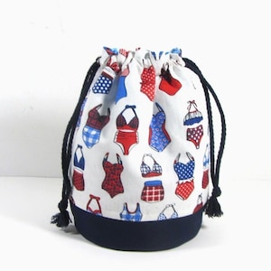 Peut inclure: Sac à cordon blanc avec une bordure bleu marine. Le sac est décoré d'un motif de maillots de bain rouges, bleus et blancs.