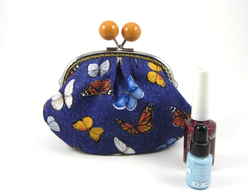 May include: A small blue fabric coin purse with a metal clasp and wooden knobs. The purse is decorated with a pattern of colorful butterflies on a dark blue background.