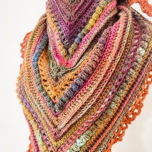 May include: A handmade, colorful crochet shawl in a triangular shape. The shawl features a variety of colors, including pink, orange, purple, and green, with a textured stitch pattern. The edges are finished with a decorative, scalloped border.