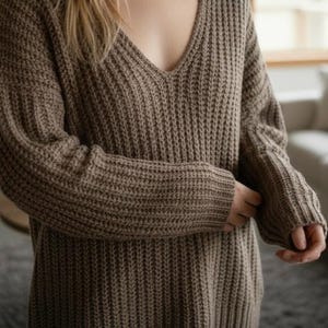 May include: A brown, oversized sweater with a deep V-neck. The sweater has a thick, ribbed knit texture and long sleeves. The sleeves are cuffed at the wrists. The sweater appears to be made of a soft, warm material.