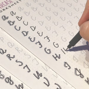 May include: A close-up of a worksheet with uppercase letters printed in gray. A hand is tracing the letter "H" with a black pen. The worksheet is titled "uppercase worksheet".