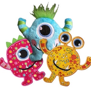 May include: Three plush toy monsters with big eyes. One is blue with green hair, one is pink with white polka dots, and one is yellow with a swirl pattern.