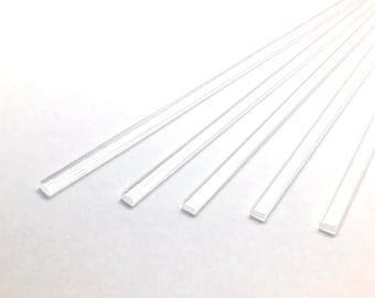 May include: Six clear acrylic rods, each with a square cross-section, are arranged in a fan shape on a white surface.