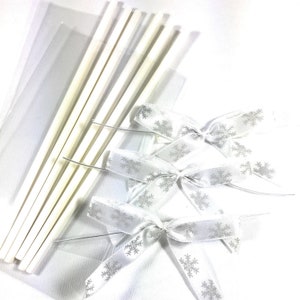 May include: Three white satin bows with silver snowflake patterns and six white craft sticks in a clear plastic bag.