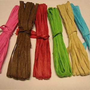 May include: Assortment of six paper raffia ribbons in various colors, including pink, brown, red, green, beige, and blue. The ribbons are tied together in the middle.