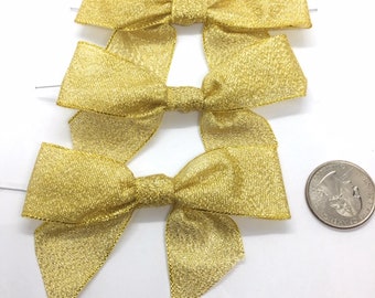 May include: Three gold glitter wired bows, each approximately 2 inches wide, with a shiny, textured finish. The bows are arranged in a stack, with the top bow slightly offset from the others. A US quarter is included for size reference.
