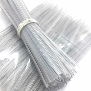 May include: A bundle of white plastic twist ties, also known as cable ties, are wrapped together with a white rubber band. The ties are in a clear plastic bag.