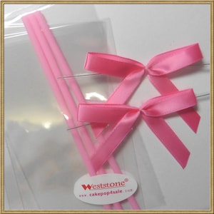 May include: A package of pink cake pop sticks and pink satin bows. The package includes three sticks and two bows. The package is labeled "Weststone" and "www.cakepop4sale.com".
