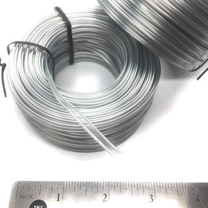 May include: Two spools of silver-colored wire, each about 3 inches in diameter, are shown next to a ruler. The wire is wound tightly around each spool.