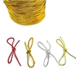 May include: A spool of gold metallic cord sits above four decorative bows in red, gold, silver, and gold. The bows are tied with the same metallic cord. The image is on a white background.