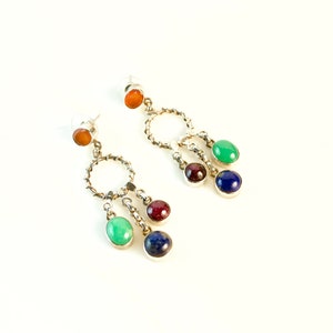 Peut inclure: Une paire de boucles d'oreilles pendantes en argent avec un motif circulaire et trois pierres précieuses chacune. Les pierres précieuses sont vertes, rouges et bleues.
