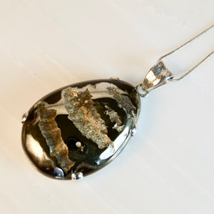 Peut inclure: Un collier en chaîne argent avec un pendentif en forme de larme orné d'une pierre d'agate noire et blanche avec des accents argentés.