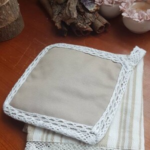 Può includere: Un set di due asciugamani da cucina beige con bordino in pizzo bianco. L'asciugamano superiore è in tessuto beige con bordino in pizzo bianco e il testo "Rose Garden" stampato nell'angolo. L'asciugamano inferiore è in tessuto a righe bianco e beige con bordino in pizzo bianco.