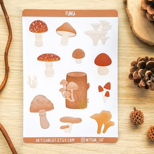 A sticker sheet featuring digitally illustrated fungi / mushrooms in warm tones. The sticker sheet is laid out on a wooden table surrounded by natural props such as pinecones, wood slices & a twig