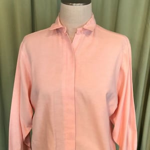 May include: A long-sleeved, light pink button-down shirt with a collared neckline.