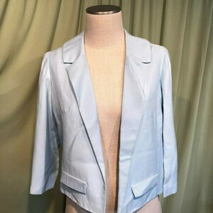 May include: A light blue blazer with a notched collar and long sleeves. The blazer has a cropped length and two pockets.