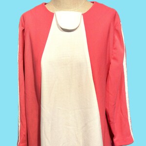 May include: A coral-colored dress with a white panel down the center. The dress has long sleeves with a white stripe down the side and a round neckline. The dress is displayed on a mannequin.