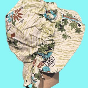 May include: A vintage-style bonnet in cream with a floral and leaf pattern in shades of green, brown, and blue. The bonnet features a ruffled brim and ties, offering a classic, feminine aesthetic. The fabric has a subtle striped texture.