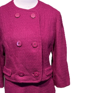 Op de afbeelding: Een magenta wollen rokpak met een dubbelrijg jasje en vier grote knopen.