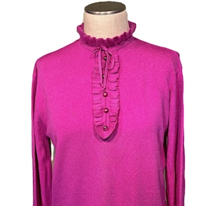 May include: A magenta long-sleeved sweater with a ruffled neckline and a row of buttons.