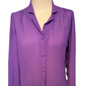 Op de afbeelding: Een lang mouw, paarse blouse met knopen en een kraag.