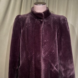 May include: A purple faux fur jacket with a stand-up collar and a single button fastening. The jacket has a slightly fitted silhouette and long sleeves.