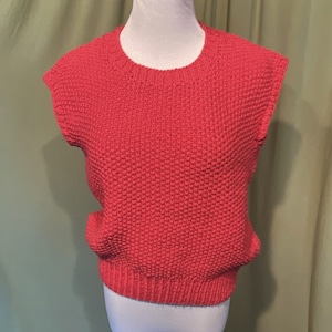 May include: A sleeveless, red knitted sweater with a round neckline.