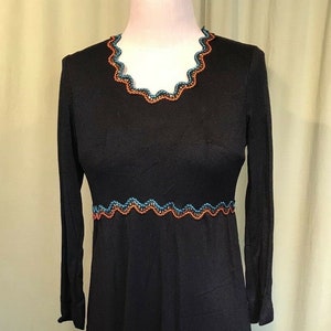 May include: A long black dress with a scalloped neckline and hem. The neckline and hem are trimmed with orange and blue embroidery.