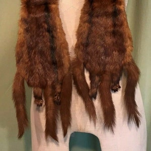 May include: A brown fur scarf, displayed on a mannequin. The scarf is made of long, soft fur with a rich, dark brown colour. The ends of the scarf have the shape of animal paws. A white tag with the numbers "819" and "17" is attached.