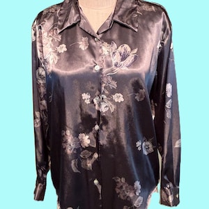 May include: A dark gray satin button-down shirt with a floral pattern in shades of white and gray. The long-sleeved shirt has a classic collar and buttoned cuffs. The floral design is spread across the shirt.