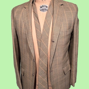 May include: A brown plaid blazer and matching tie displayed on a mannequin. The blazer has a classic two-button closure and front pockets. The tie is patterned with a similar plaid design. The mannequin has text that reads "NORMAL MODEL FORM, INC. N.Y."