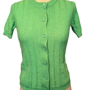 May include: A green short-sleeved cardigan with a button-up front and two pockets.