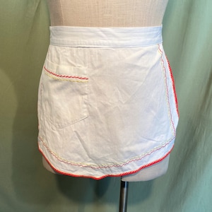 May include: White apron with a scalloped edge and red, yellow, and white stitching. The apron has a single pocket on the front.