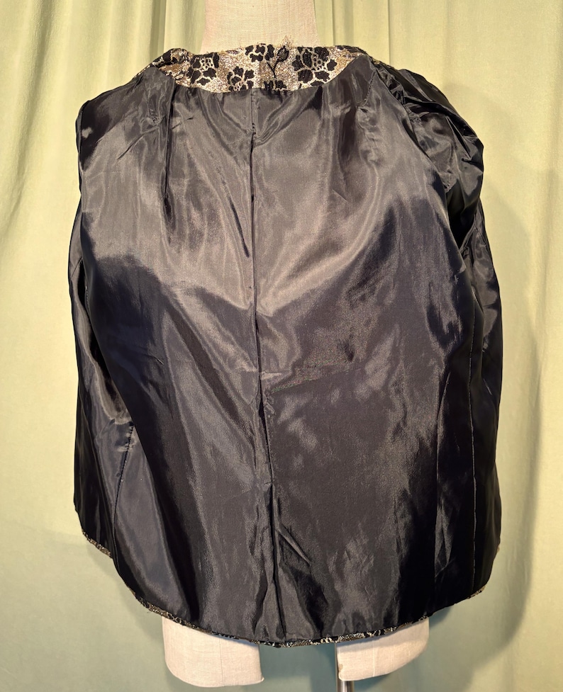 May include: A black jacket with a gold and black floral pattern on the collar and hem.