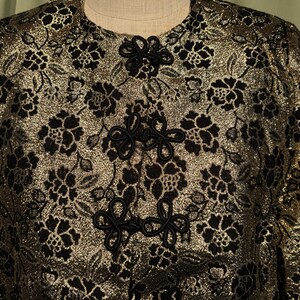 May include: A gold brocade jacket with black floral embroidery and black knotted closures.