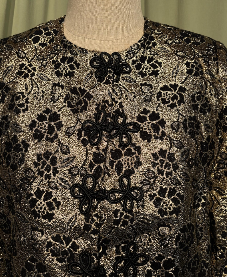 May include: A gold brocade jacket with black floral embroidery and black knotted closures.