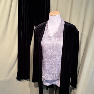 Puede incluir: Un traje de pantalón de terciopelo negro con una blusa plateada brillante. El traje tiene una chaqueta larga y pantalones rectos.