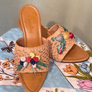May include: A pair of brown straw heeled sandals with floral embellishments. The sandals have a woven design and are decorated with colorful flowers and leaves. The brand name "Cass Country" is visible on the insole.