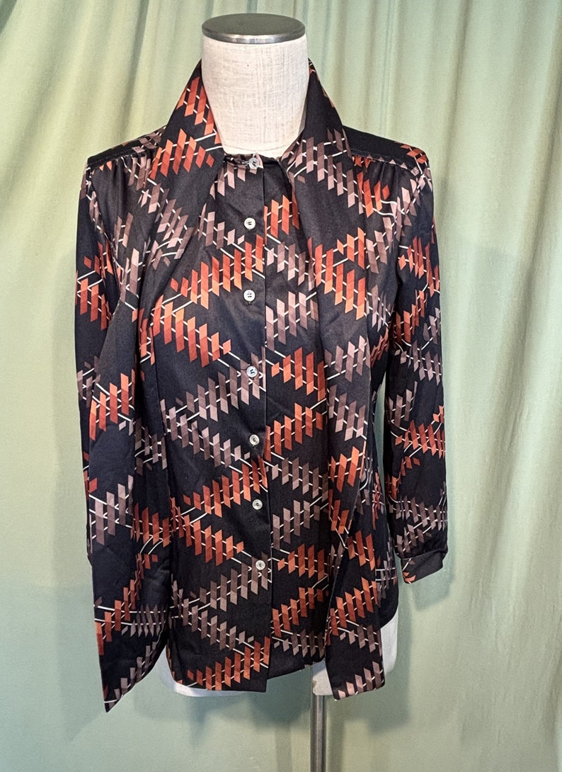 Op de afbeelding: Een zwart lang mouw overhemd met knopen en een geometrisch patroon in bruine en oranje tinten.