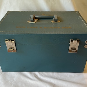 May include: A teal blue vintage sewing machine carrying case with two silver latches and a silver handle. The case has the text "SINGER PARTS & SUPPLIES" printed on the top.