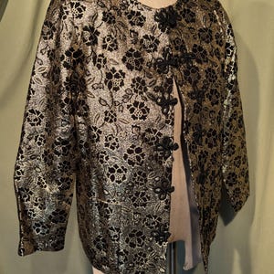 May include: A gold and black brocade jacket with a mandarin collar and black knotted closures. The jacket has a floral pattern.