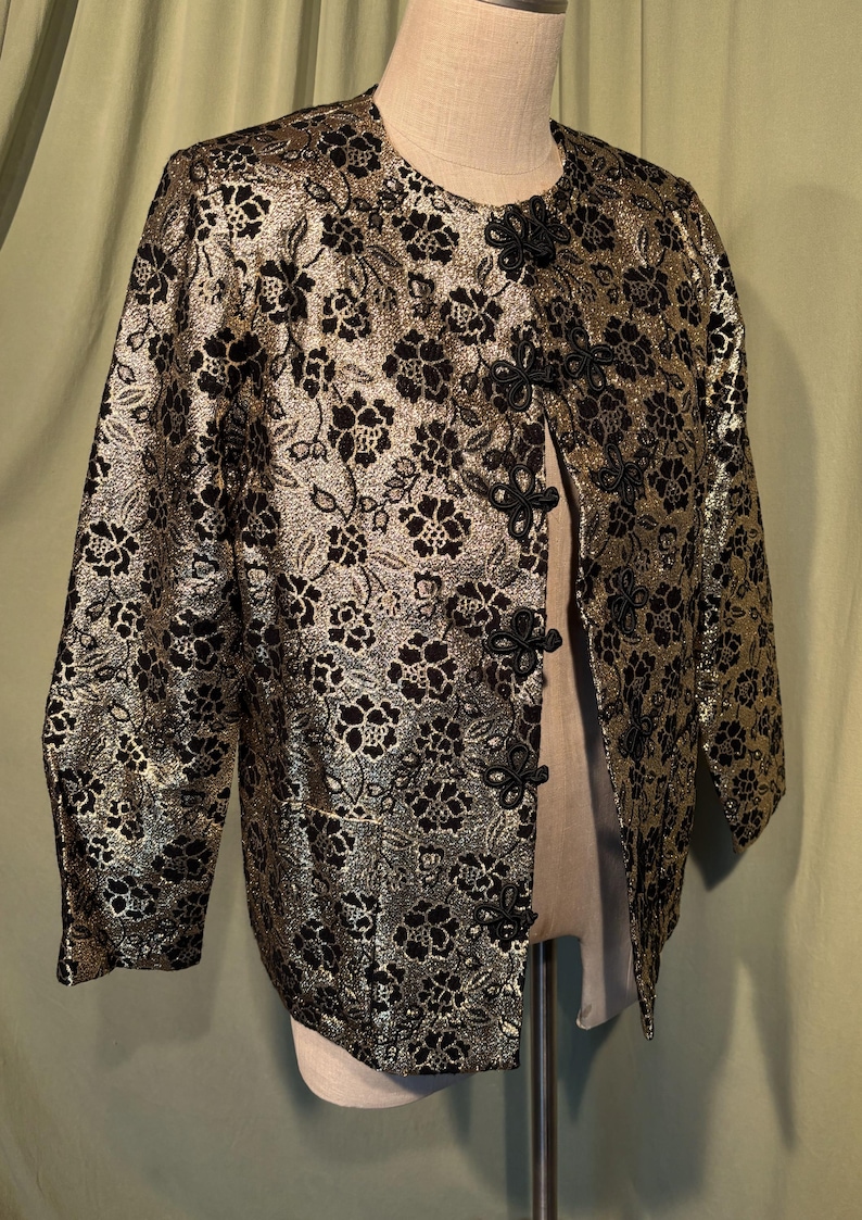 May include: A gold and black brocade jacket with a mandarin collar and black knotted closures. The jacket has a floral pattern.