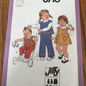 May include: Simplicity sewing pattern number 8716 for toddler clothing. The pattern includes three designs: a blue and white dress with a vest, a brown dress with a pocket, and a red and white outfit with a vest. The pattern is labeled "Jiffy easy cut-easy sew" and includes 2-3 main pattern pieces.
