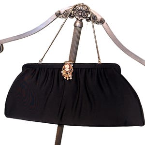 May include: A black satin evening bag with a gold clasp and a cameo brooch. The bag is hanging on a silver stand.