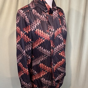 Op de afbeelding: Een zwart en bruin overhemd met lange mouwen en een geometrisch patroon. Het overhemd heeft een strik aan de hals.