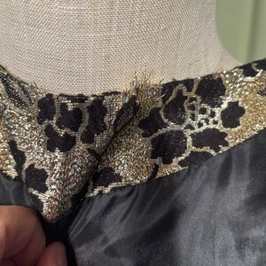 May include: Close-up of the neckline of a black dress with a gold and black floral brocade trim.