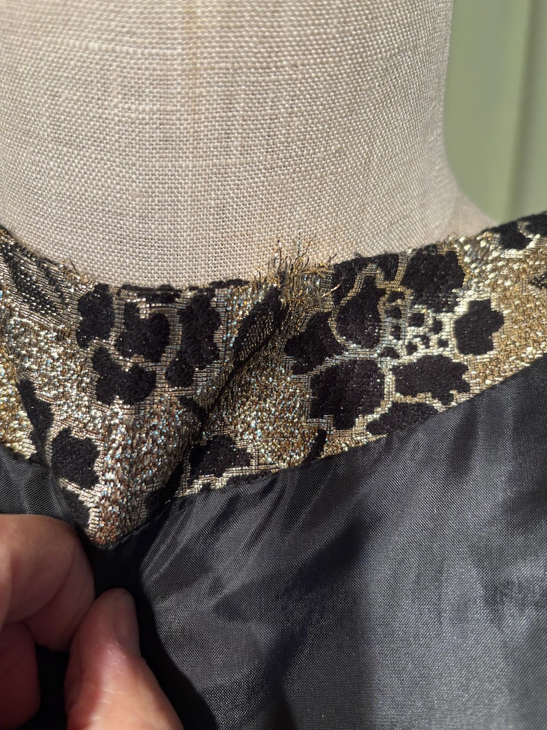 May include: Close-up of the neckline of a black dress with a gold and black floral brocade trim.
