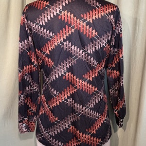 Op de afbeelding: Een lang mouw shirt met een geometrisch patroon in tinten van bruin, oranje en wit op een zwarte achtergrond.