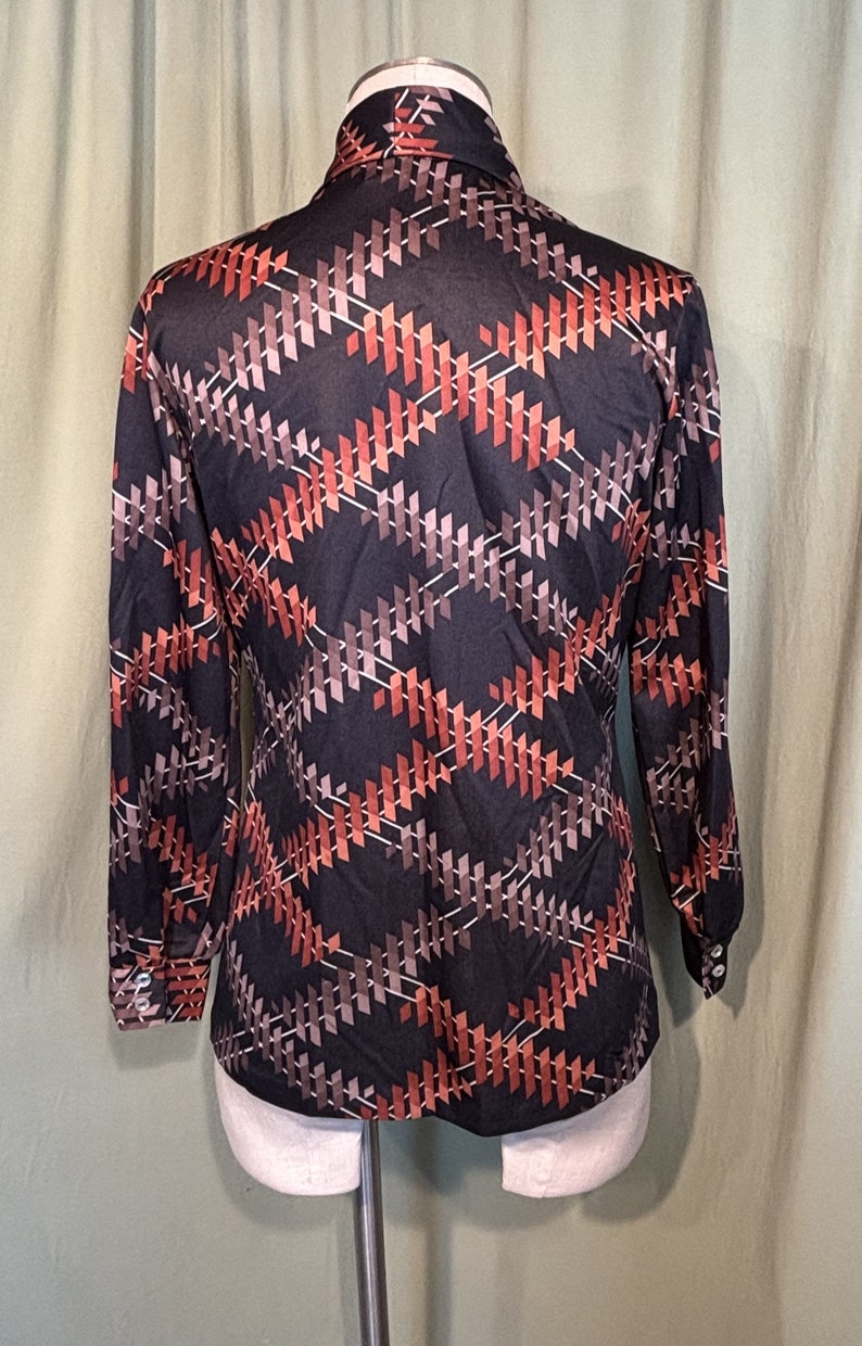 Op de afbeelding: Een lang mouw shirt met een geometrisch patroon in tinten van bruin, oranje en wit op een zwarte achtergrond.